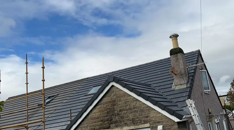 Stone bungalow with a newly tiled dark grey roof and chimney, scaffolding still in place