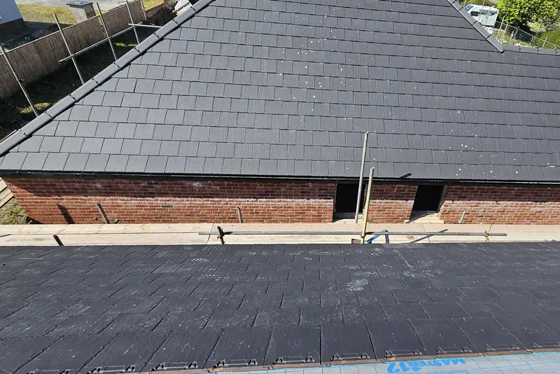 New dark slate-effect roof on a brick new-build, with a second roof slope in the foreground