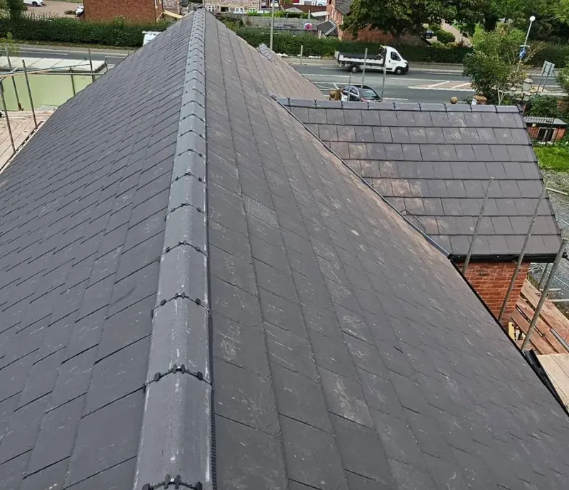 New dark tiled hipped roof with a dry-fixed ridge, seen from the scaffold