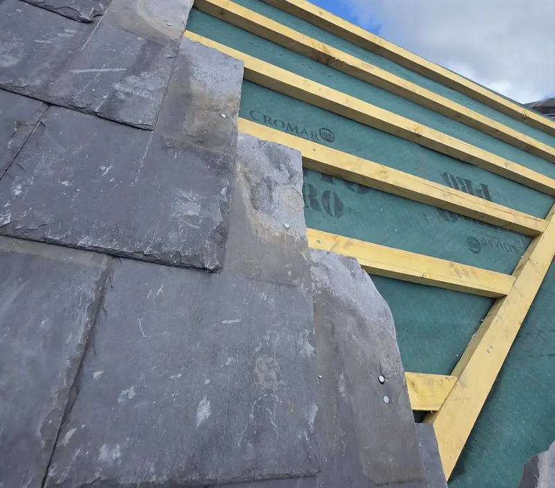 New natural slates being laid over green roofing membrane and timber battens