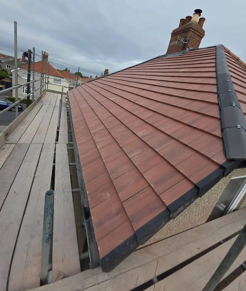Newly reroofed house: red flat tiles, a grey dry-fixed hip and a brick chimney, seen from the scaffolding