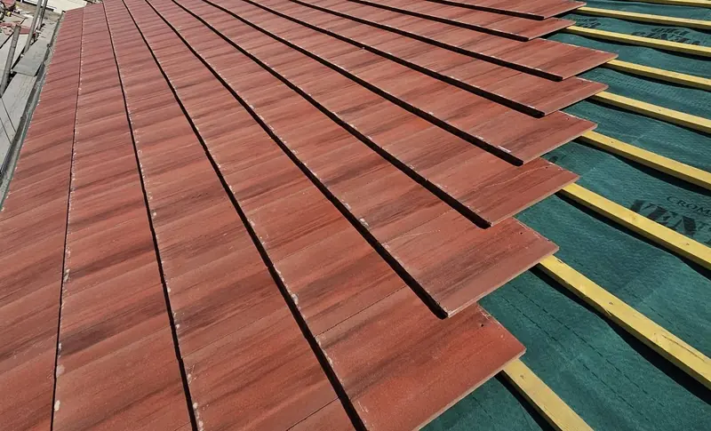 New red flat interlocking tiles being laid in courses over the green membrane and battens