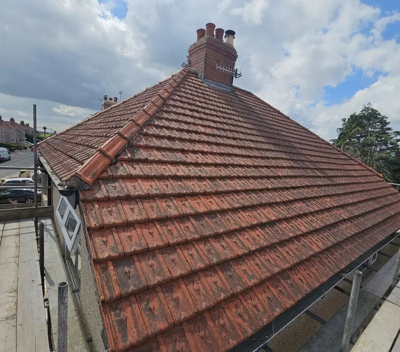Hipped roof covered in old, weathered red concrete tiles with scaffolding around it before a reroof