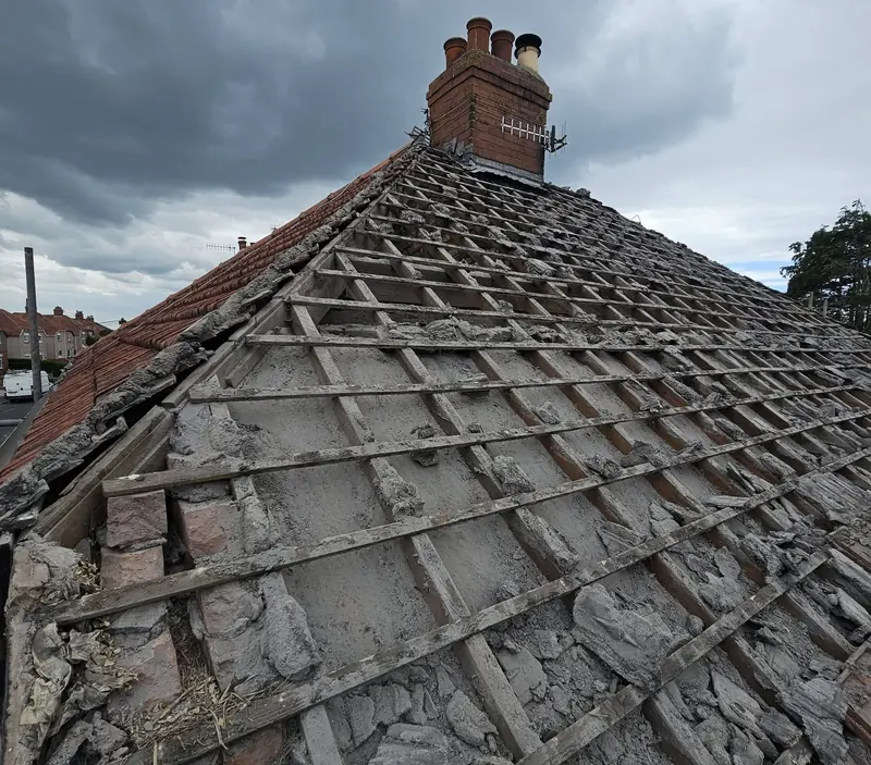 The same roof with the tiles removed, showing old battens and crumbling mortar below the chimney